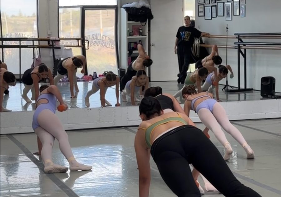 Alumnas en un ejercicio de acondicionamiento en el piso del salón, frente al espejo.